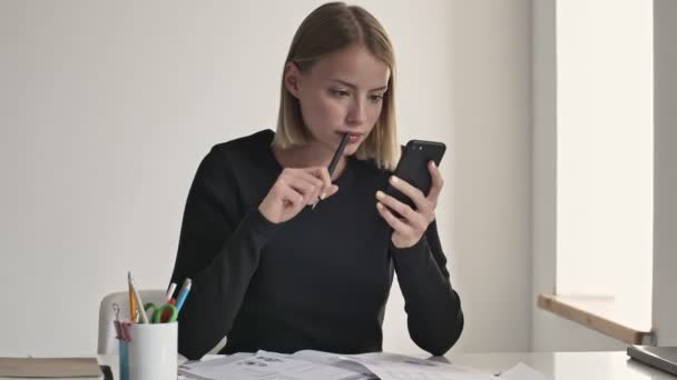 Hoş Genç Sarışın Bir Kadın Beyaz Bir Ofiste Akıllı Telefonunu — Stok video