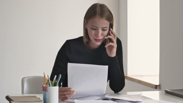 Een Glimlachende Jonge Blonde Zakenvrouw Praat Aan Telefoon Terwijl Werkt — Stockvideo