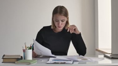 Sarışın, ciddi bir iş kadını beyaz bir ofiste çalışırken kâğıt döküman kusuyor.