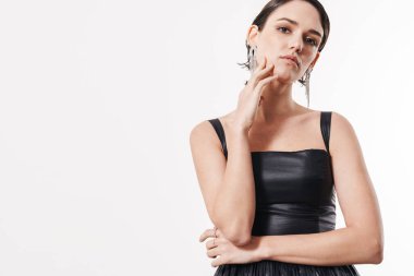 Siyah kokteyl elbisesi giyen çekici genç esmer kadın beyaz arka planda izole bir şekilde kameraya bakıyor.