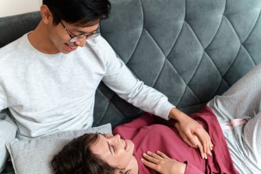 Romantik çok uluslu çiftin evdeki kanepede gülümseyip konuştuğu bir fotoğraf.