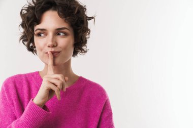 Memnun kıvırcık kadının sessiz bir jest yaptığı ve beyaz arka planda izole edilmiş bir kenara baktığı görüntüsü.