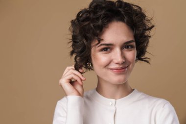 Gülümseyen ve bej arka planda izole edilmiş kameraya bakan neşeli genç bir kadın görüntüsü