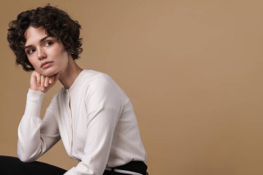 Güzel bir kadının bej arka planda tek başına otururken yan baktığı görüntüler.