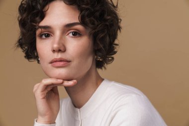 Güzel bir kadının bej arka planda izole edilmiş poz verirken ve kameraya bakarken görüntüsü