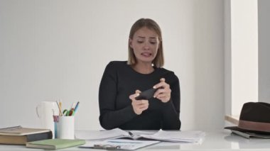 Duygusal genç bir sarışın kadın, beyaz bir ofisteki masada oturan akıllı telefonuyla oyunu kaybetti.