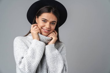 Neşeli, iyimser, şapkalı, gri duvar arkasında izole edilmiş genç bir kadının görüntüsü..