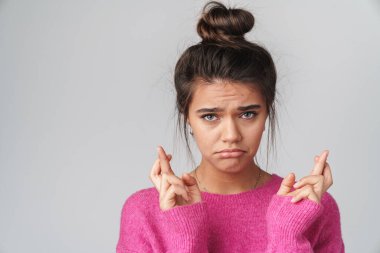 Pembe kazaklı, üzgün, güzel bir kadının beyaz arka planda parmakları çapraz pozu.