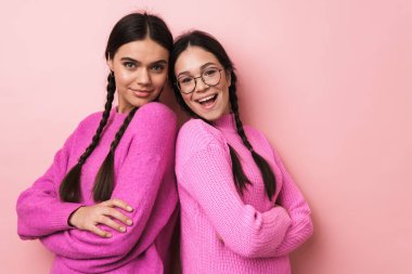 Pembe arka planda sırt sırta duran iki neşeli genç kız.