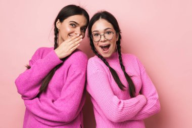 Gayri resmi giyinmiş, pembe arka planda birlikte dedikodu yapan iki mutlu genç kızın görüntüsü.