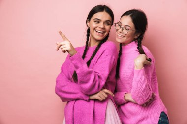 Örgülü iki genç kızın resmi kenara bakıyor ve pembe arka planda izole edilmiş telif alanını işaret ediyor.