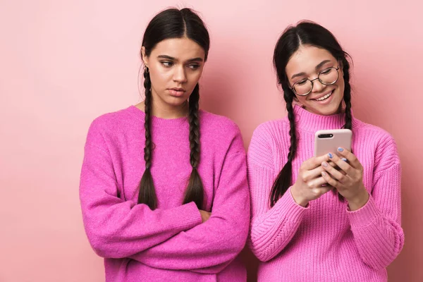 画像の動揺十代の女の子立っていますによって彼女の幸せな女性友人とともに携帯電話絶縁上のピンクの背景 — ストック写真