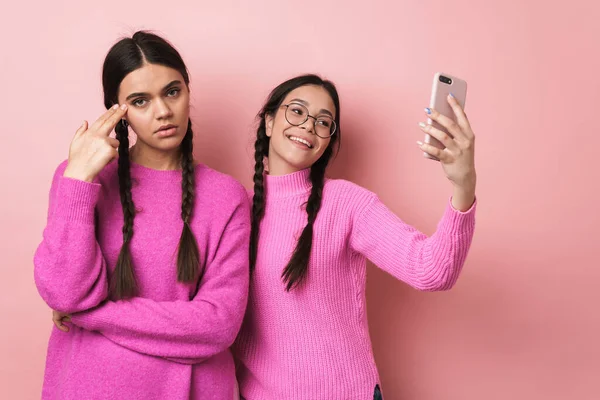 照片中 心烦意乱 生气的少女站在她快乐的女友身边 与粉色背景的手机隔离在一起 — 图库照片