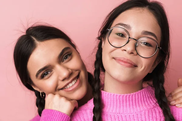Pembe arka planda izole edilmiş, günlük kıyafetleriyle kameraya gülümseyen iki mutlu genç kızın görüntüsü.