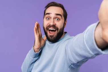 Şok olmuş genç bir adamın fotoğrafı. Mor arka planda izole edilmiş. Kamerayla selfie çek..