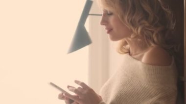 Evde cep telefonu kullanan pozitif sarışın kadın.