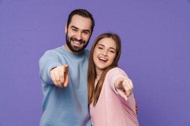 Mor arka planda izole edilmiş mutlu, genç bir çiftin fotoğrafı sizi işaret ediyor..
