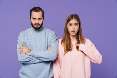 Şok olmuş bir kızın, mor arka planda izole edilmiş, gücenmiş bir erkek arkadaşı işaret etmesi..