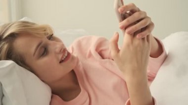Evde yatakta cep telefonu kullanan güzel, iyimser bir kadın.
