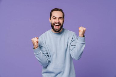 Image of a handsome positive happy young man isolated over purple wall background showing winner gesture. clipart