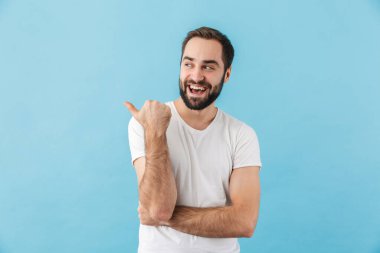 Mavi arka planda izole bir şekilde duran ve fotokopi çeken, mutlu, sakallı ve tişört giyen genç bir adamın portresi.