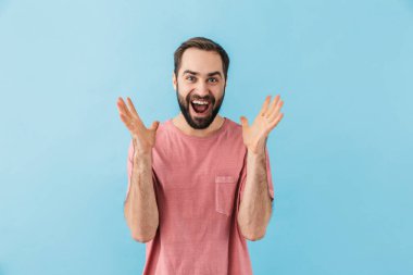 Mavi duvar arkasında izole edilmiş genç, yakışıklı, heyecanlı, çığlık atan adamın görüntüsü.