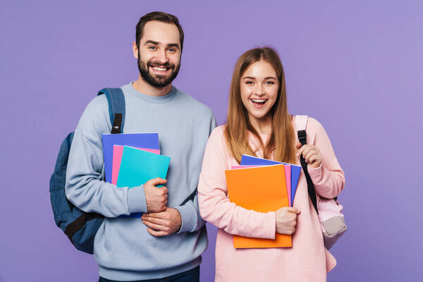 Photo of a positive happy loving couple friends students isolated over purple wall background holding books.