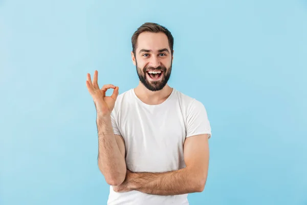 一个年轻而快乐的 兴奋的留着胡子的男人穿着T恤 孤零零地站在蓝色背景下 摆出一副不错的姿势的画像 — 图库照片