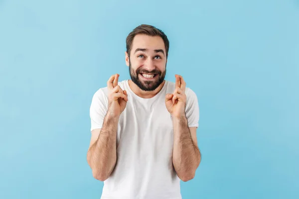 青の背景に孤立立ってTシャツを着て若い陽気な興奮ひげを生やした男の肖像画 保持指幸運のために交差 — ストック写真