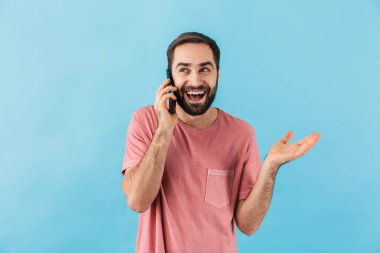Mavi duvar arkasında izole edilmiş, cep telefonuyla konuşan genç, yakışıklı, iyimser bir adamın görüntüsü.