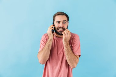 Mavi duvar arkasında izole edilmiş, cep telefonuyla konuşan genç ve kafası karışmış bir adam görüntüsü.