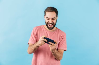 Mavi duvar arkasında izole edilmiş genç, yakışıklı, mutlu bir adamın resmi cep telefonuyla oyun oynuyor..