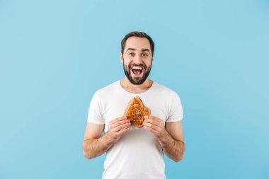 Mavi arka planda tek başına duran, mutlu, heyecanlı, sakallı ve tişört giyen genç bir adamın portresi.