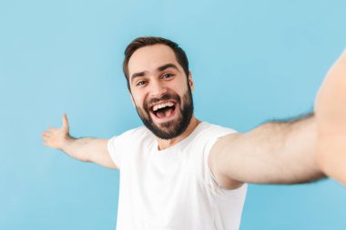 Mavi duvar arkasında izole edilmiş heyecanlı neşeli genç bir adam görüntüsü. Kamerayla selfie çek..