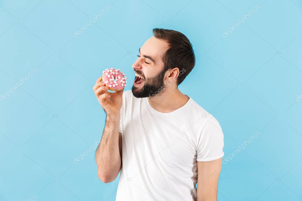 Photo of young happy positive man isolated over blue wall background with donut.