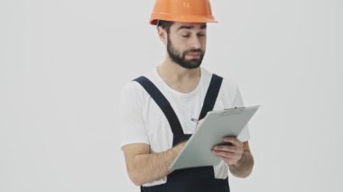 Genç sakallı bir inşaatçının beyaz duvar arkasında kask takıp not yazması ciddi bir düşünce..