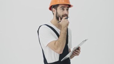 Düşünceli, konsantre olmuş, sakallı bir adam. Beyaz duvar arkasında, kask panosuna notlar yazarak izole edilmiş..