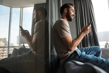 Evde cep telefonu kullanan mutlu, iyimser bir gencin resmi..