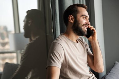 Evde cep telefonuyla konuşan neşeli bir gencin resmi..