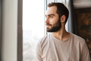 Yakışıklı, sakallı bir adam. Evinin penceresinde dikiliyor, başka tarafa bakıyor.