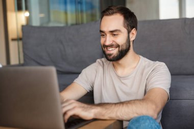 Evde dizüstü bilgisayar kullanan mutlu iyimser bir gencin görüntüsü..