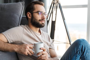 Evde kahve içen, gözlüklü, konsantre bir gencin görüntüsü..