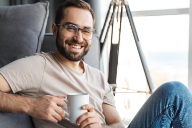 Evde kahve içen neşeli genç bir adamın görüntüsü..