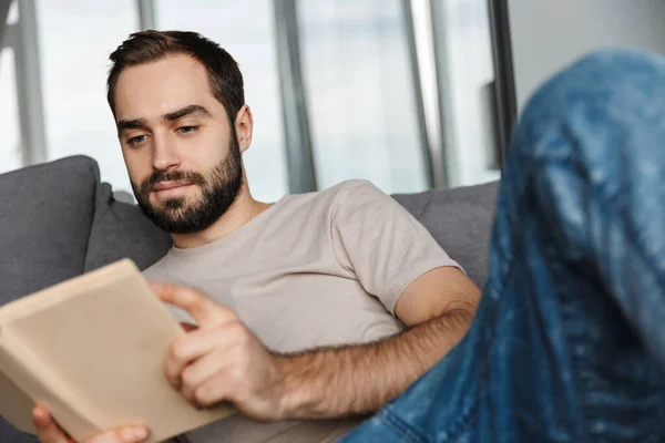 Foto Homem Bonito Sério Concentrado Casa Livro Leitura Sofá — Fotografia de Stock