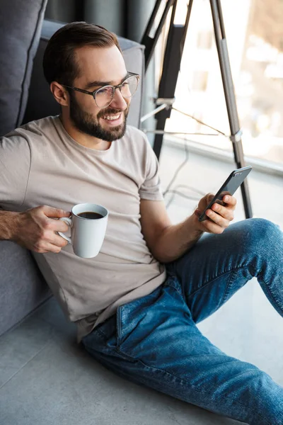 Foto Jovem Positivo Dentro Casa Bebendo Café Usando Telefone Celular — Fotografia de Stock