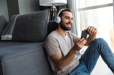Evde oturmuş, kulaklıkla müzik dinleyen gülümseyen genç bir adamın görüntüsü..