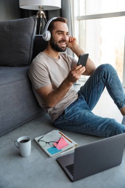 Evde oturup kulaklıkla müzik dinleyen mutlu ve iyimser bir gencin görüntüsü yerde oturup cep telefonuyla sohbet ediyor..