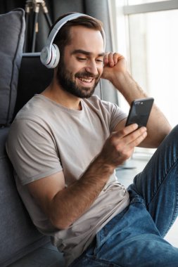 Evde oturmuş, kulaklıkla müzik dinleyen gülümseyen genç bir adamın görüntüsü..