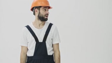 Kafası karışmış genç sakallı adam miğferiyle beyaz duvar arkasına izole edilmiş..