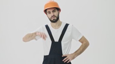 Yorgun genç sakallı adam miğferiyle beyaz duvar arkasında izole edilmiş.